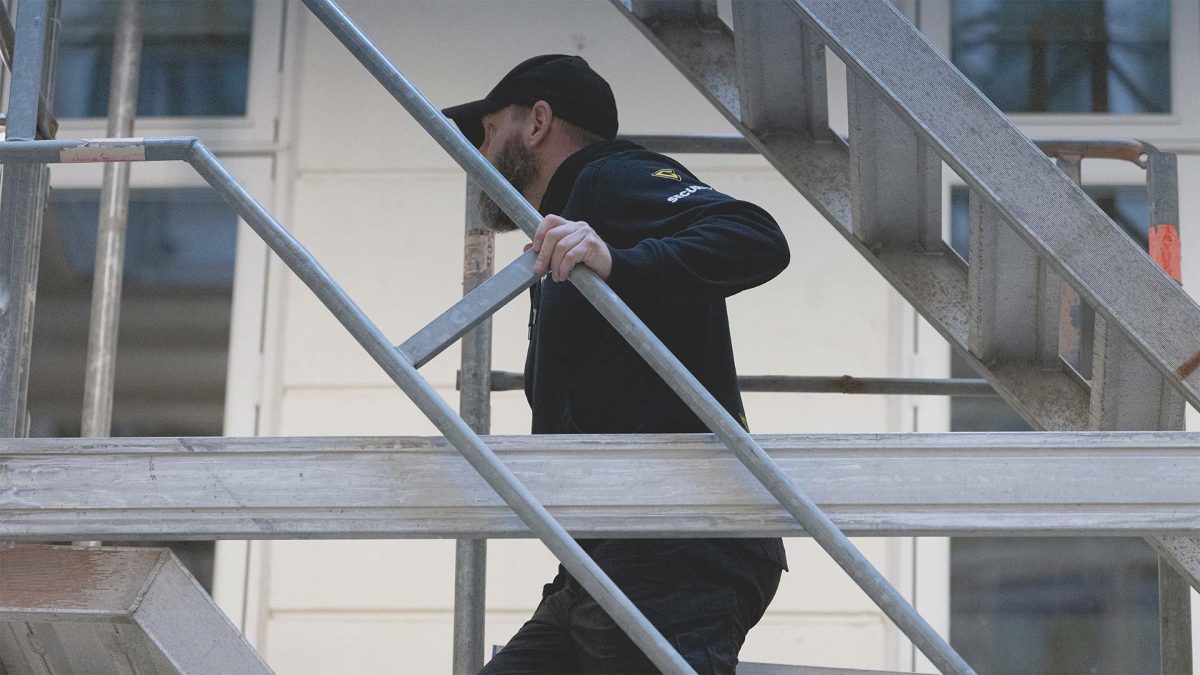 En vagt i uniform på en byggeplads klatrer op ad en metaltrappe.