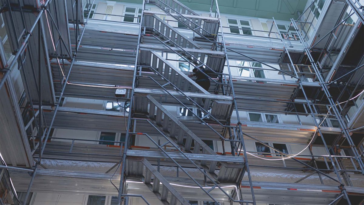En vagt i uniform går op ad en trappe i en bygning med stilladser for at sikre sikkerheden.