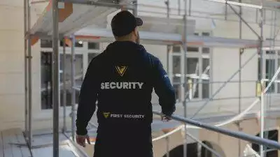 En vagt i en uniform, står på stilladset på en byggeplads og kigger ud over pladsen.