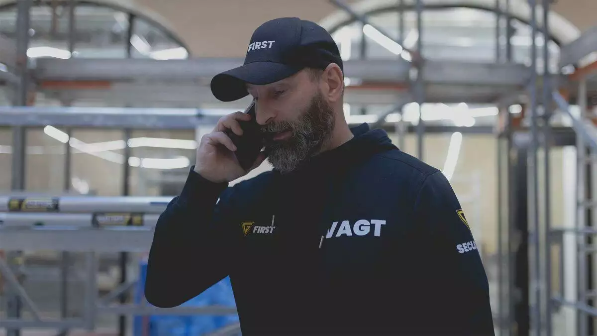 En skægget vagt i uniform taler i mobiltelefon på en byggeplads.